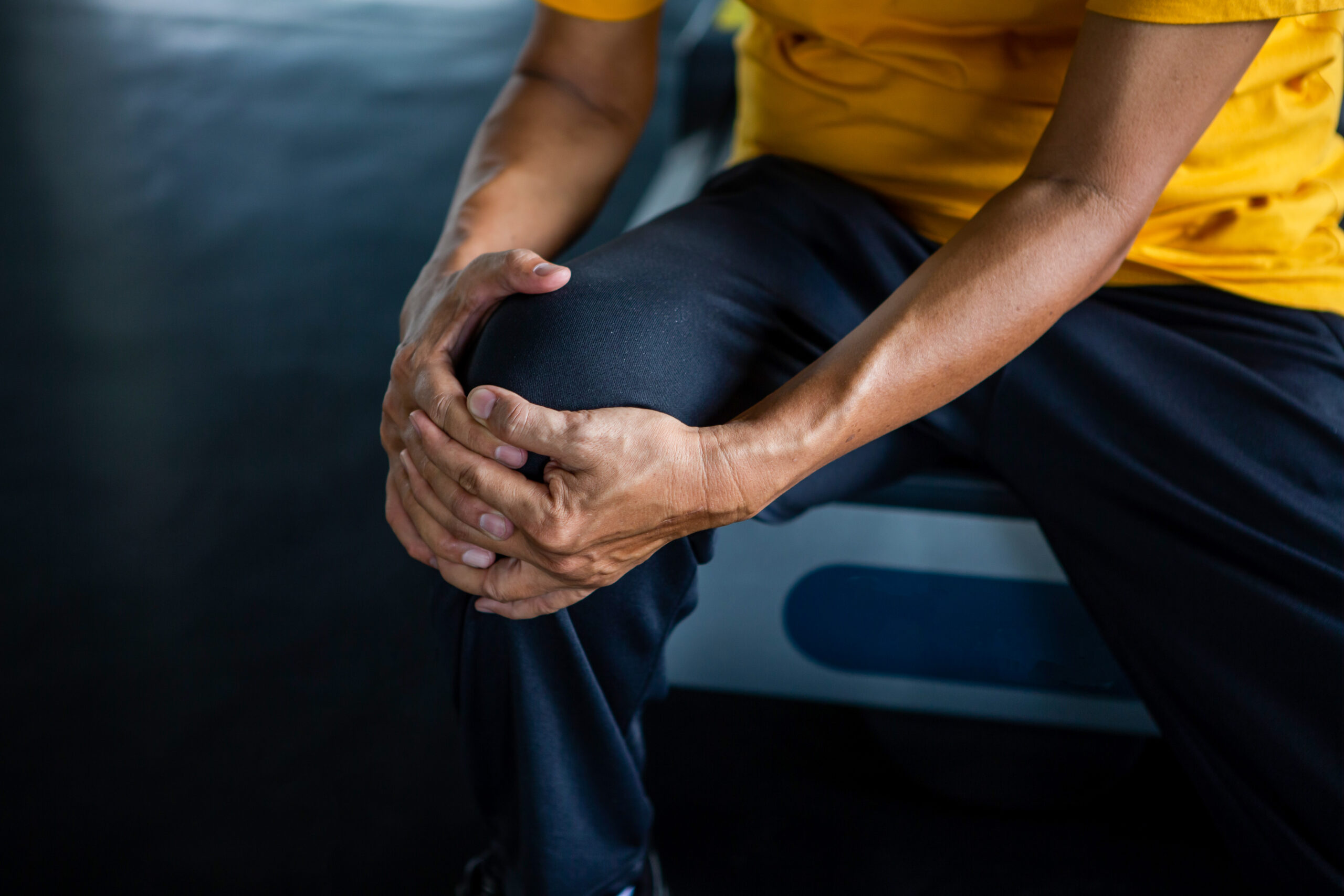 Senior Asian sport man injury knee pain sitting on treadmill in fitness gym . aged suffering from Arthritis elder male exercising , workout, training ,healthy ,Retirement ,older, close up